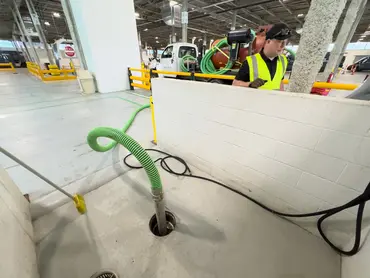  Biolein technician vacuuming a catch basin drain inside a covered vehicle service facility 