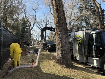  Biolein technician in protective suit operating a hydrovac hose at a gated residential driveway 