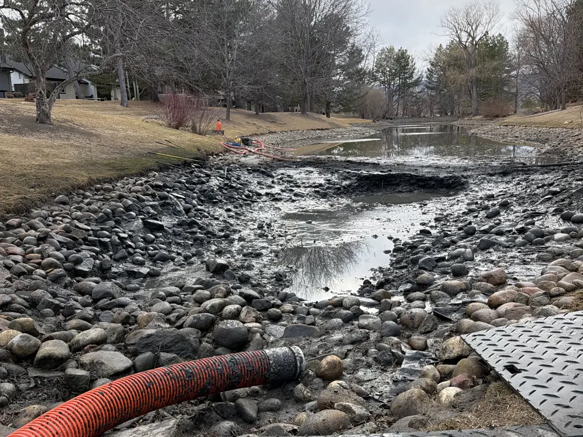 Sediment removal hose along the rocky bank of a partially drained Colorado pond Sediment removal hose along the rocky bank of a partially drained Colorado pond